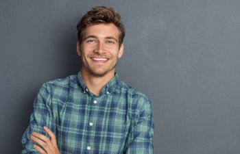 Broadly smiling young man standing with his arms folded