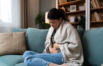 Stomach ache, cramps and hands of woman with abdomen pain due to constipation, menstruation or ibs issue. Sick, home and person suffering and holding belly in a house lounge, couch and living room